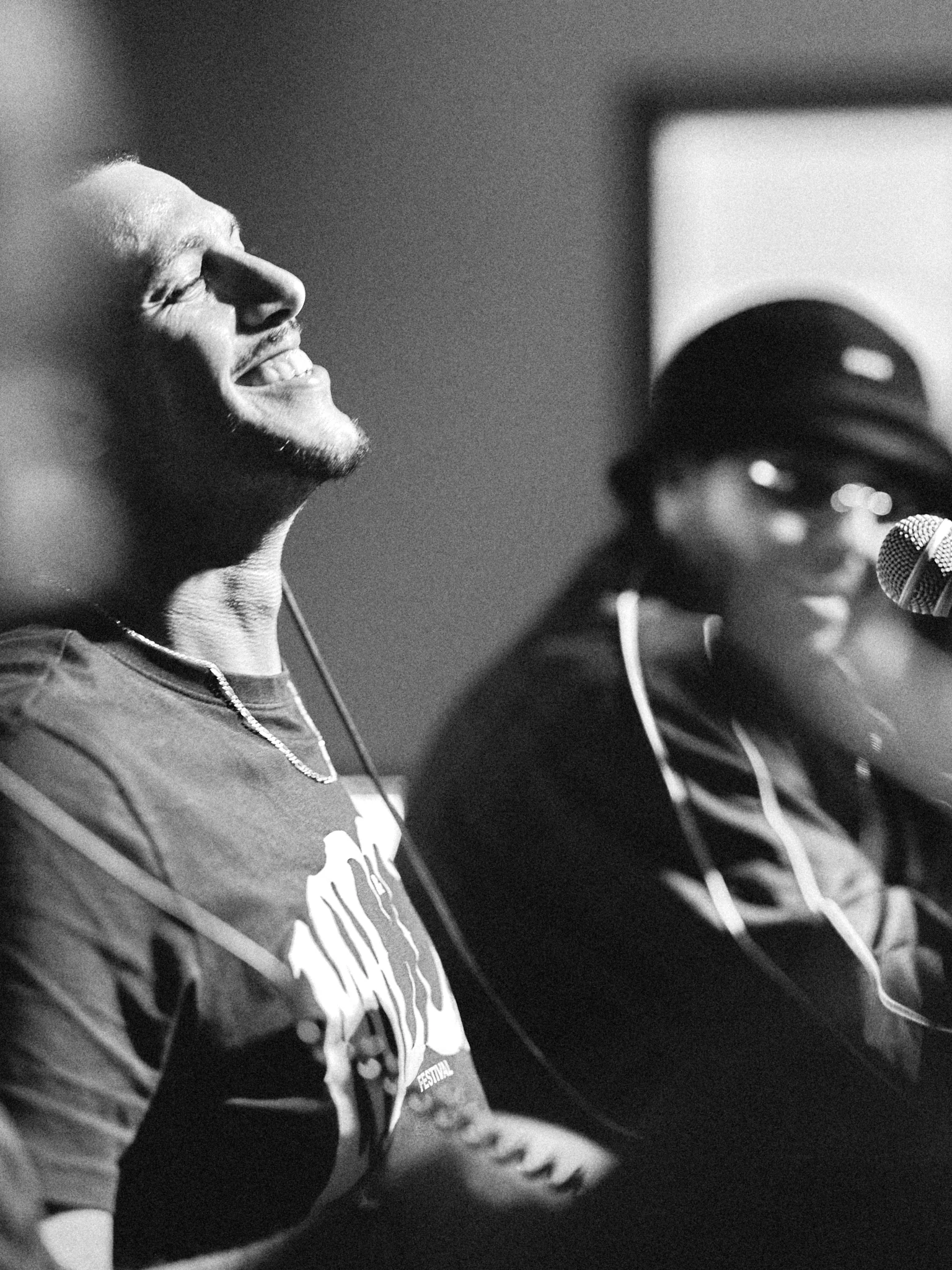 Rappeur éclatant de rire, tête en arrière, à côté d'un autre participant, noir et blanc