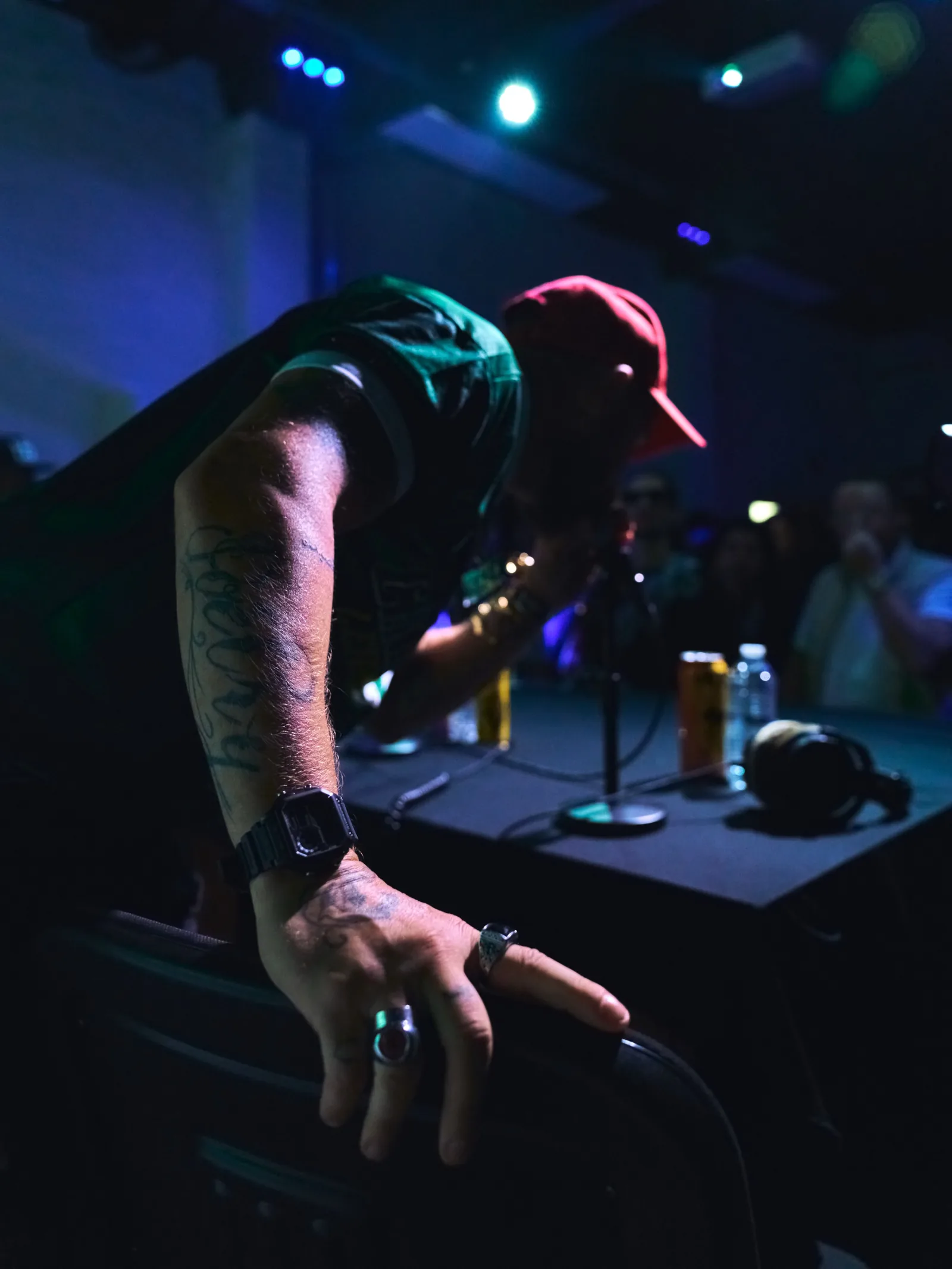 Rappeur penché vers la table, tatouages et montre au poignet, ambiance bleue de la salle, Mulhouse